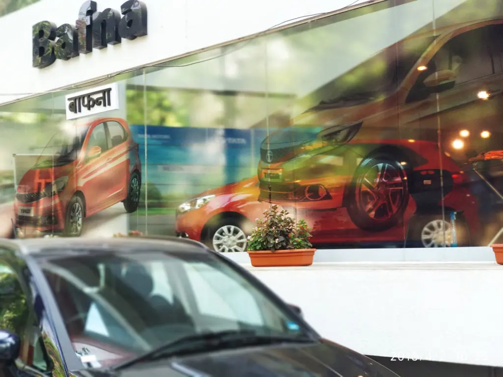 transparent window vinyl pasted on the glass front of a car outlet shows an image of a red car and also allows you to look inside the showroom