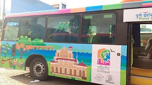 Side view of a Pune Darshan bus covered with printed vehicle graphics depicting scenes of historical monuments in Pune