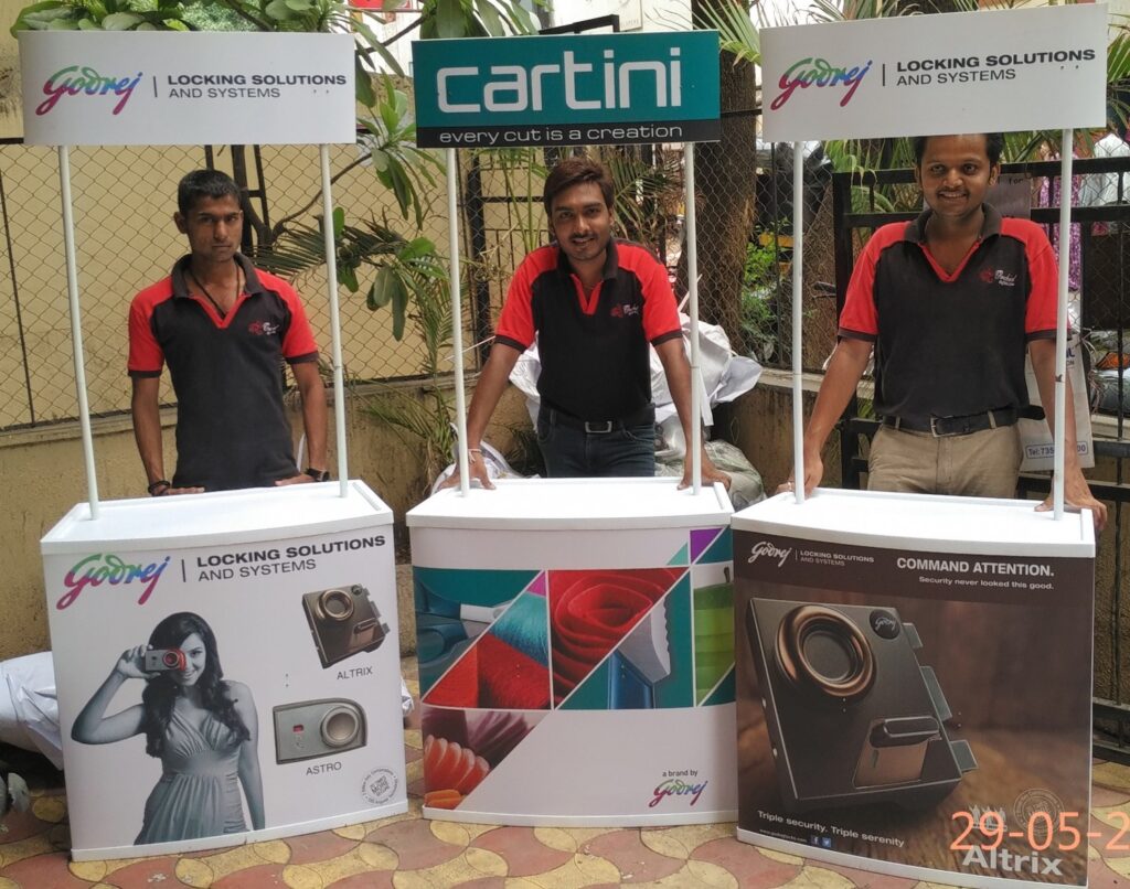 Three exhibition promo tables branded with product images and salesmen standing behind