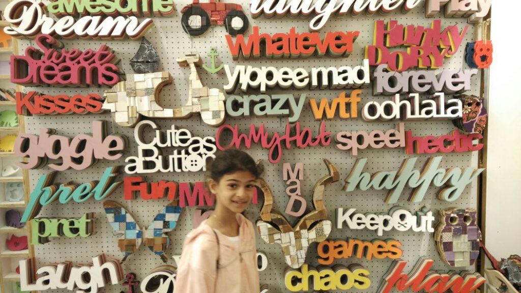 Letter wall décor made of scores of artistically designed words made of wood with a young girl posing in front