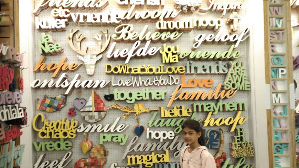 Young girl standing in front of a 3D wall mural made of letters and words of different colours cut on a CNC router