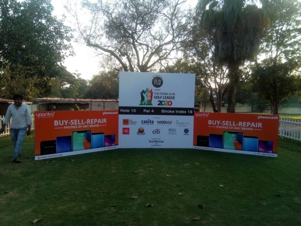 One large metal frame backdrop with two small side panels showing sponsors advertising message at a golf course event