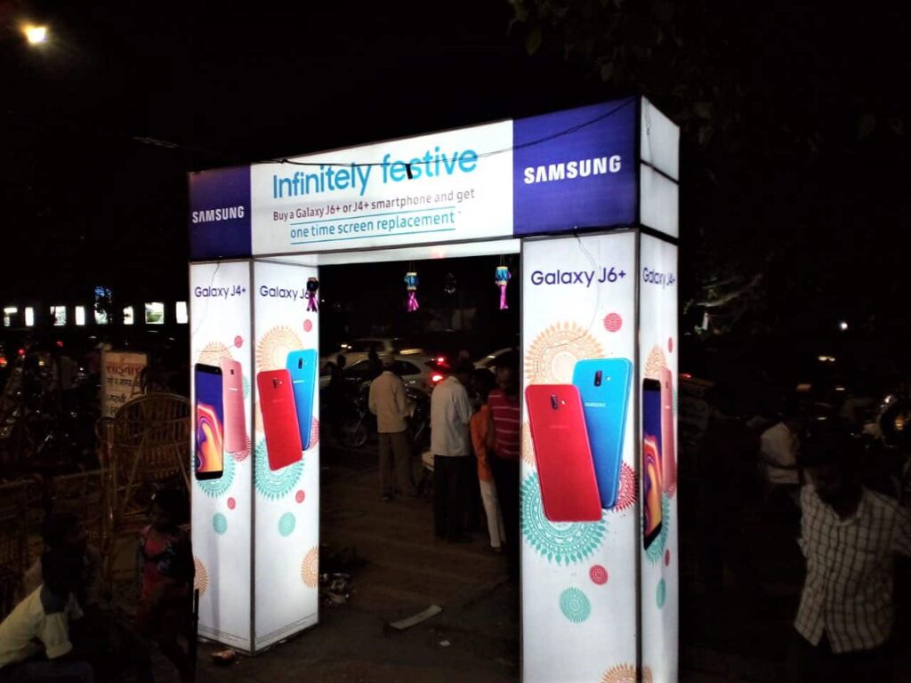 a brightly lit backlit promotional arch displaying ads for samsung mobiles installed in a crowded market place