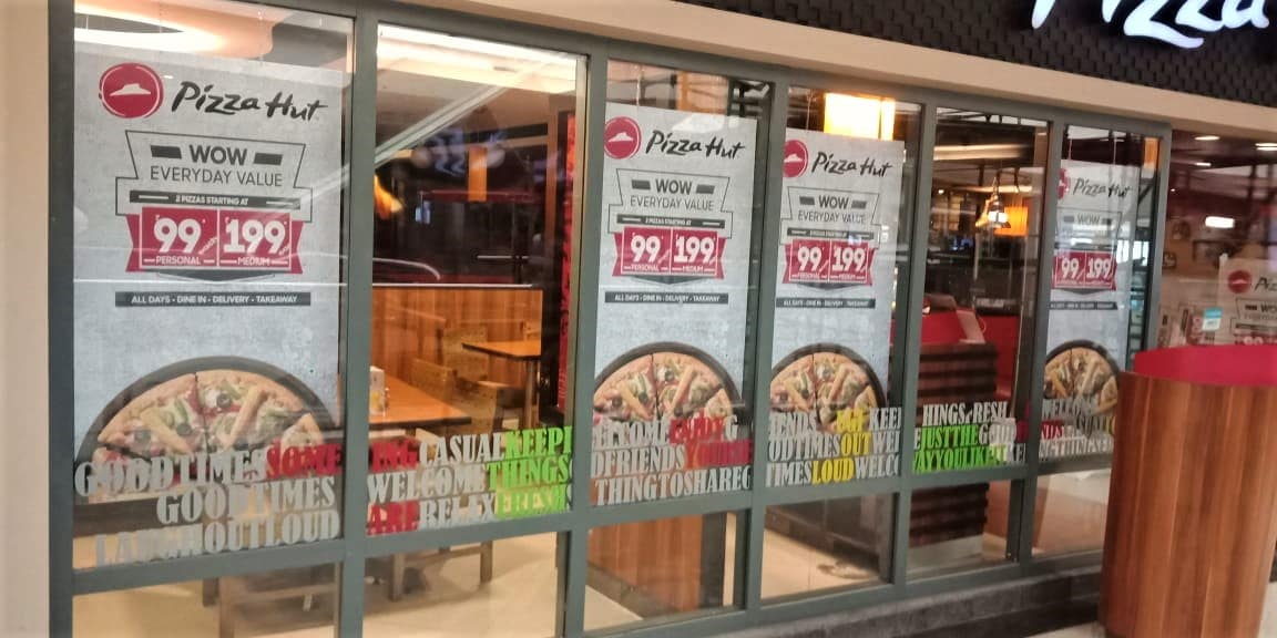 reverse glass sticker printing where the film carrying images of pizzas is pasted from inside the glass partitions at a Pizza Hut outlet