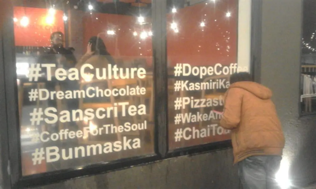 transparent glass print with letters and words in white being pasted by a fitter on the window of a cafe