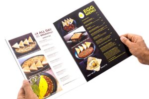 Menu card digitally printed as a booklet and held open to show food images of eggs, omelettes toast and other breakfast items