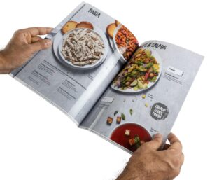 Glossy high resolution restaurant menu card printed as a booklet held open to show images of pasta salad and soups