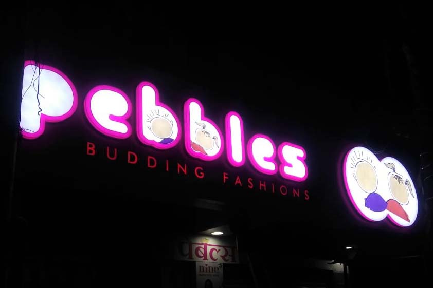 Night view of a neon glow sign board for the Pebbles garment store. Sign made of thick 3D acrylic letters in a pink and white combination and lit from within