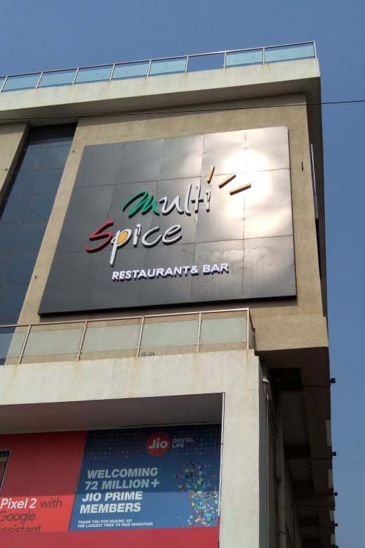 Black ACP frame installed on the side of a tall building with the Multi Spice Hotel logo on top. Logo fabricated from laser cut acrylic of different colors