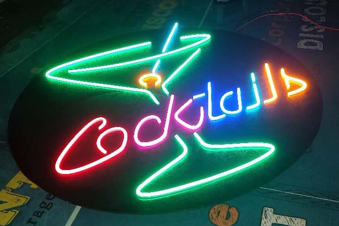 Brightly colored neon sign for a cocktail bar made out of neon lights of different colors and mounted on a black colored circular base