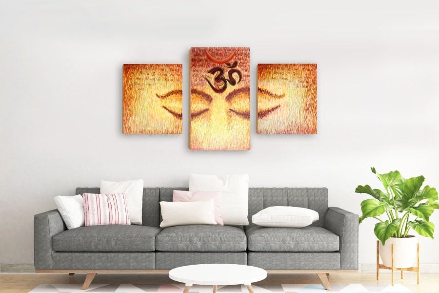 One spiritual image of eyes and the Om symbol split across three separate framed canvas prints. These prints are placed on the wall behind a sofa in a living room.