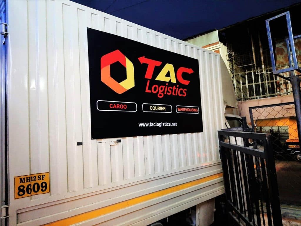 The TAC Logistics company logo printed on an ACP panel bolted on the corrugated side panel of a delivery van.
