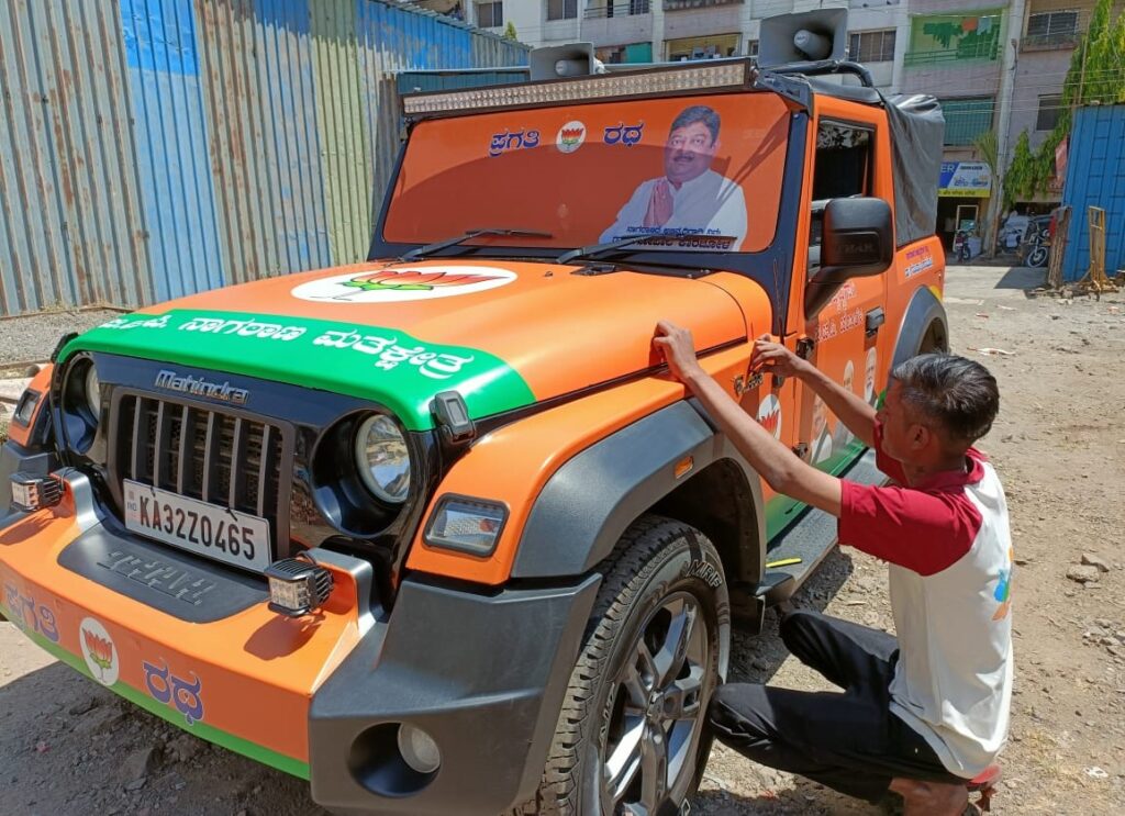 A Mahindra Thar SUV completely wrapped by custom-printed vehicle graphics showing the BJP political party's candidates, symbol, and colours very beautifully 