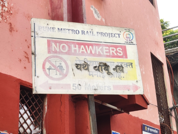 A printed signboard placed in a sunny area of a construction site with the inks faded and the sticker peeling off from the edges to make the board look extremely shabby