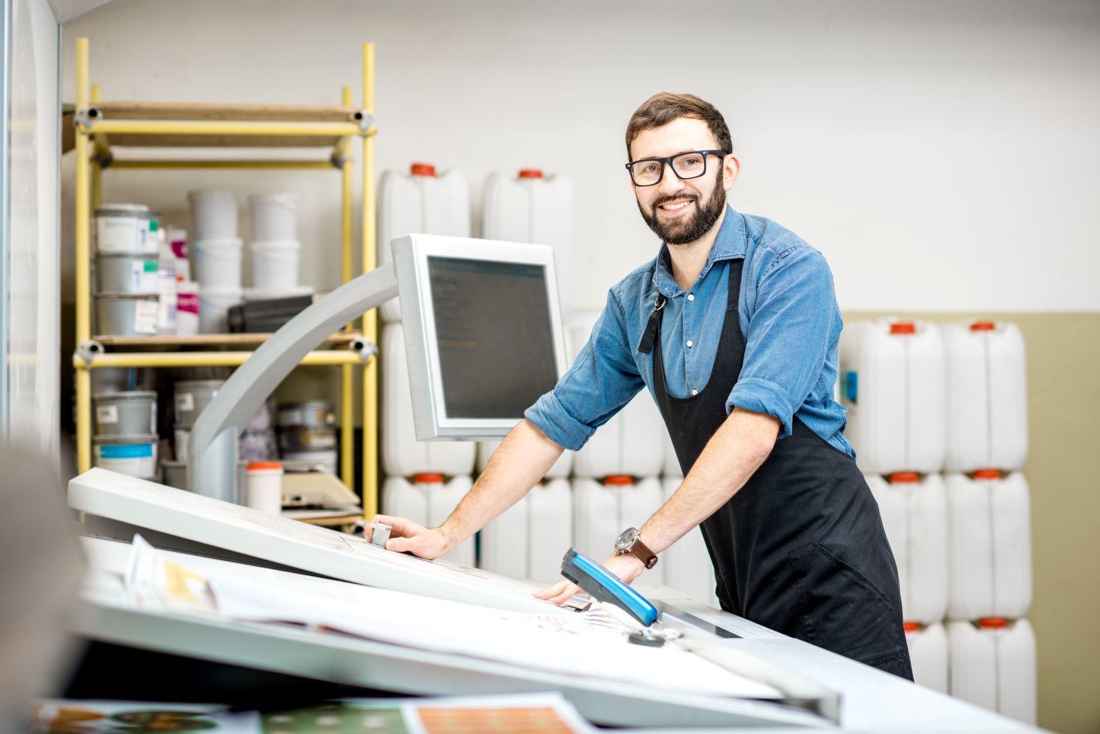 A happy and smiling male worker leaning against a digital printing press in a print shop