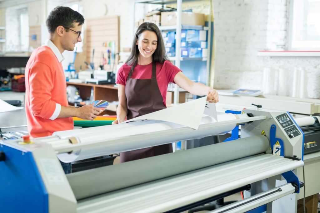 An employee and a customer in a print shop checking the colors of the print that is being reproduced on a wide format inkjet printer