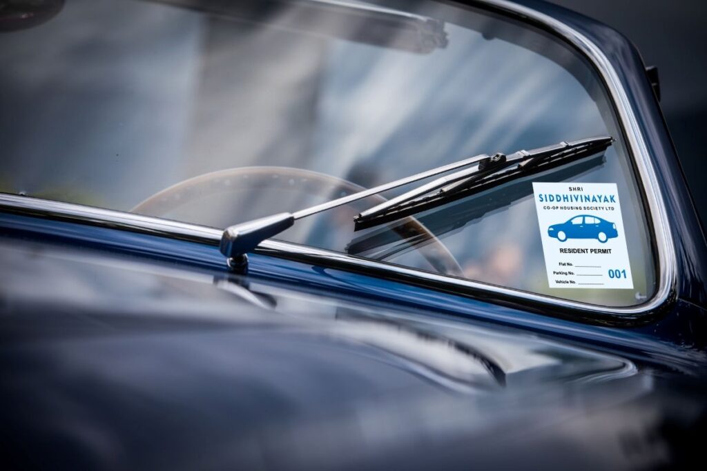The windscreen of an old car with a 4-wheeler parking sticker applied on the same, and a wiper running over the windshield