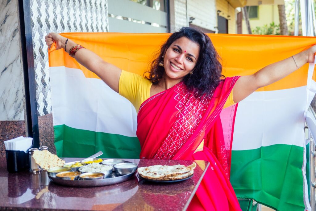 beautiful indian woman in red sari holding big indian flag behind her