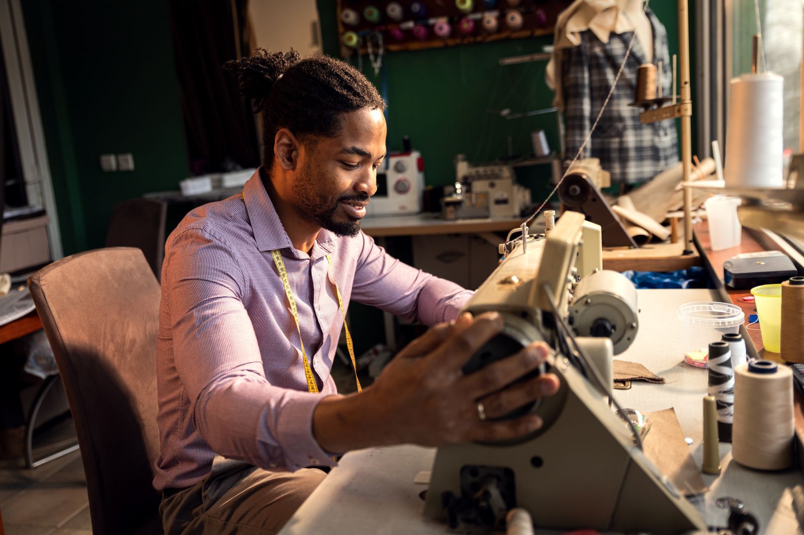 side view of a male tailor working on a sewing machine stitching a piece of fabric