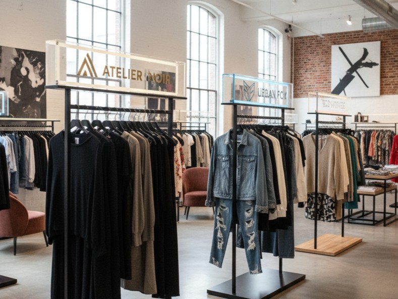A modern clothing store having different racks to display clothes from different companies and brands. Each rack also has a header plate that displays the logos of the brand of the clothing compamy. These logos are made from acrylic signs.