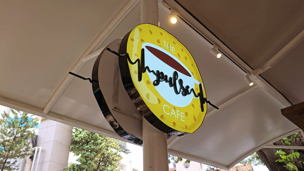 A circular logo board made of laser-cut acrylic, featuring the name ‘Pulse Cafe’ prominently displayed in 3D, with a vibrant image of a coffee cup in the background, all illuminated by bright LEDs.