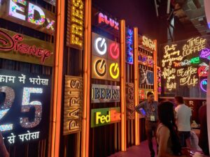 Very colourful glow sign boards made from acrylic, metal, and ACP materials, manufactured in 3D and illuminated with brightly glowing LEDs, All the logo signs are installed next to each other on a wall in a sign shop.