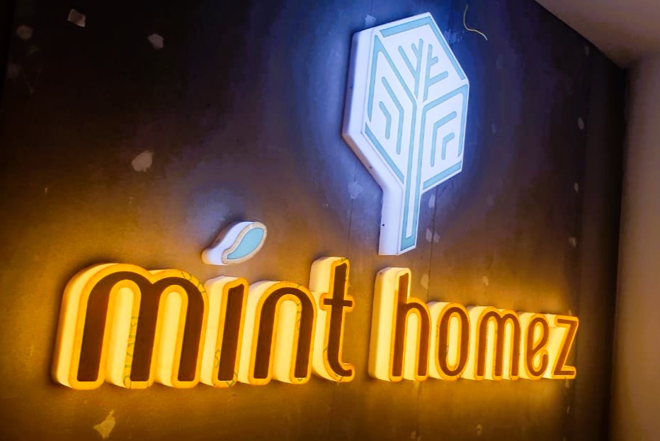 The logo for the 'Mint Homez' company is laser cut in 3D from sheets of acrylic and illuminated with embedded LEDs, fixed on a wall inside their office.