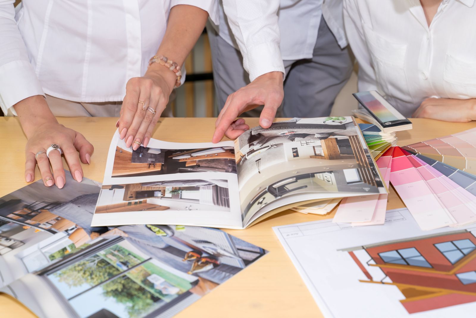 People leafing through multiple home interior design brochures spread out on a table to choose the colors and designs that they prefer