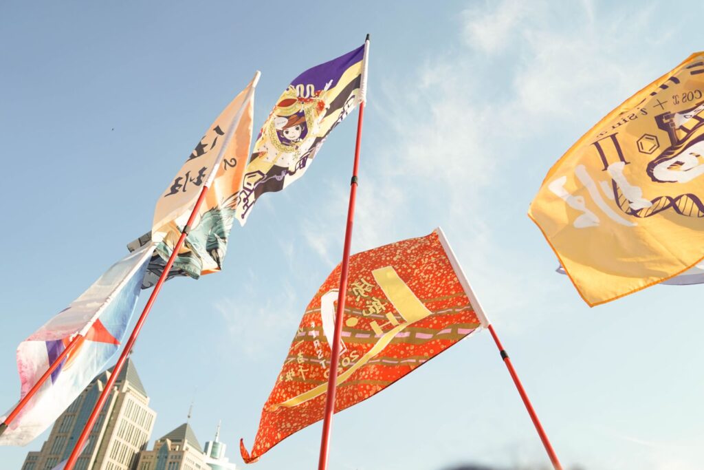 A view from the ground of flags blowing in the wind mounted high on a flagpole
