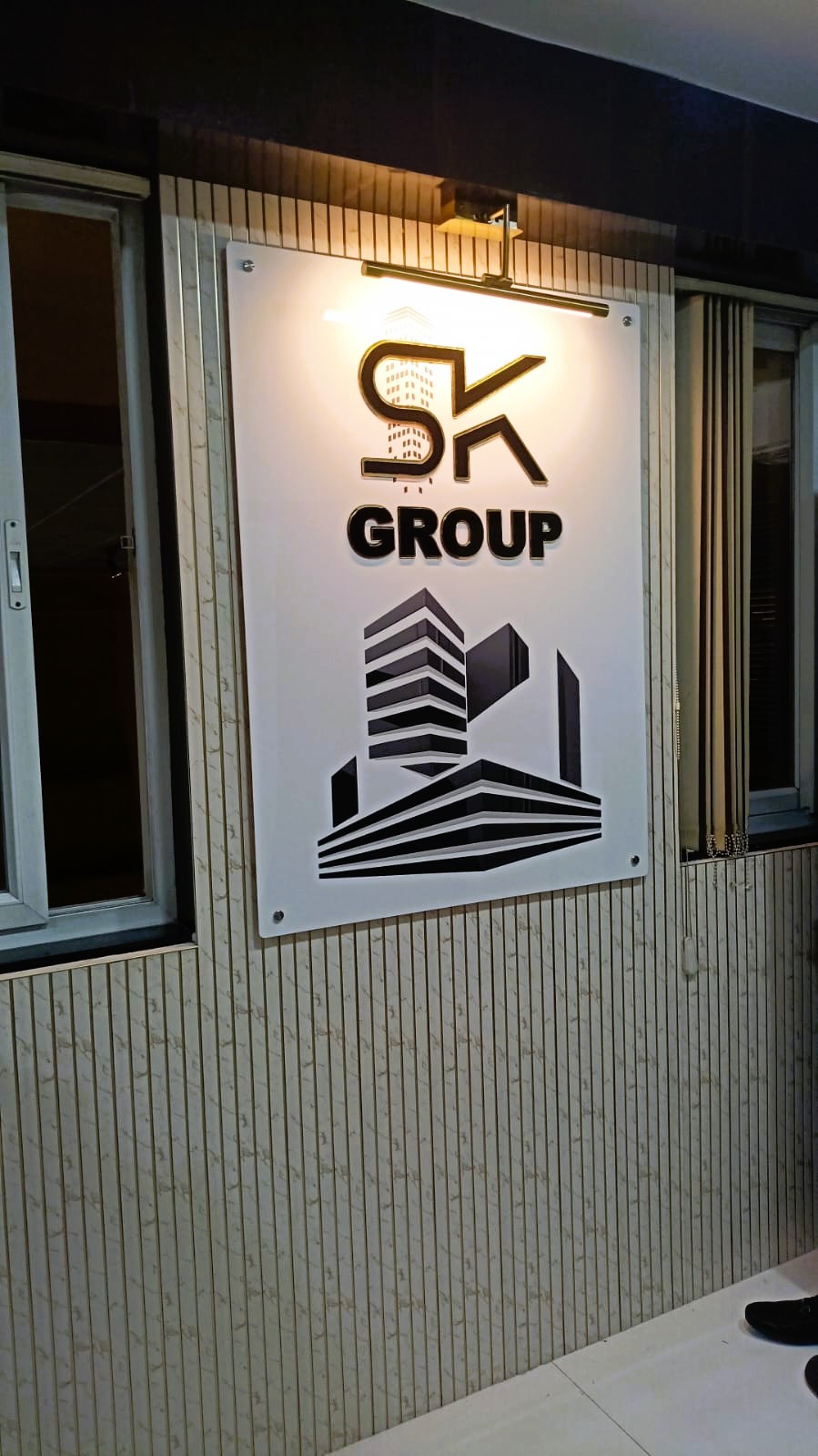 An office logo board of the sk group construction company. the laser cut acrylic signboard is made from white and black gold acrylic letters and logo mounted on a white acrylic base plate