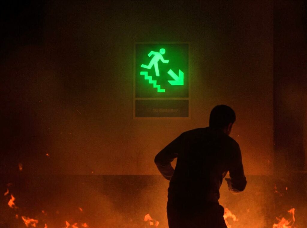 A night glow sign shining brightly in the darkness guiding a person to the closest escape route during a fire