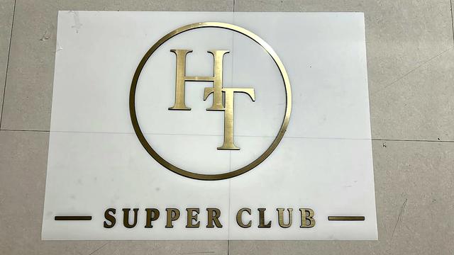 Laser-cut gold acrylic pieces of the Her Table Supper Club logo - the HT monogram, its thin circular ring and the Supper Club lettering - laid out in position on a white sheet before going up on the wall.
