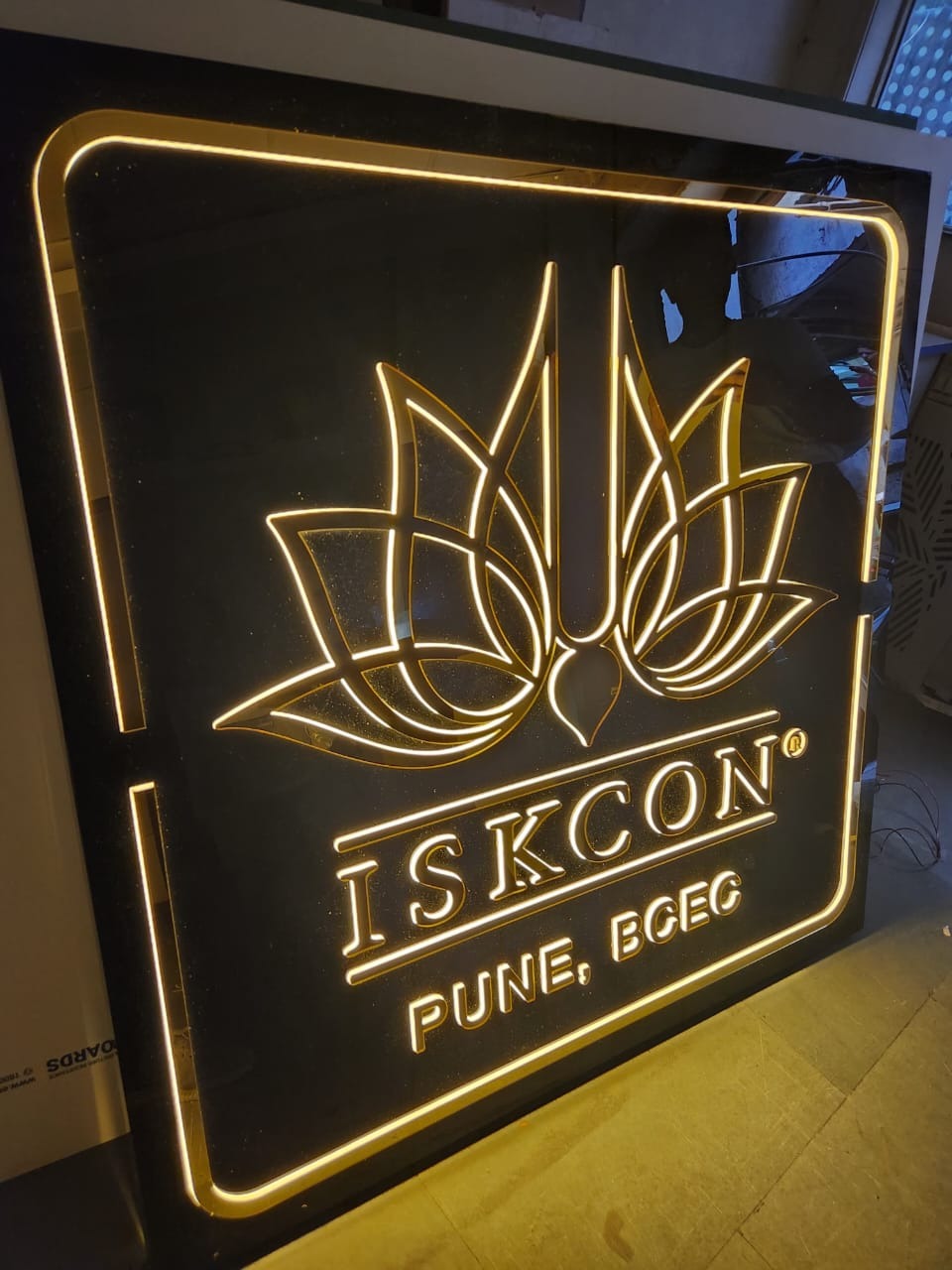 ISKCON Pune BCEC gold acrylic logo board glowing at night from LEDs hidden beneath each cut element