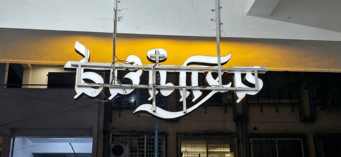 Behind-the-scenes view of the Yashogandharva channel letters showing the concealed metal pipe frame and wiring that let the sign hang without any visible support structure