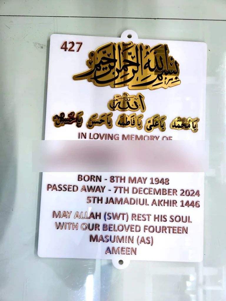 Memorial marker with gold Urdu calligraphy and mirror-finish letters on white acrylic (name blurred)