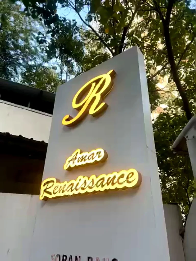 The Amar Renaissance entrance pylon at dusk: a lit rose gold R above the society’s name glowing on lit contour boxes, Sopan Baug, Pune