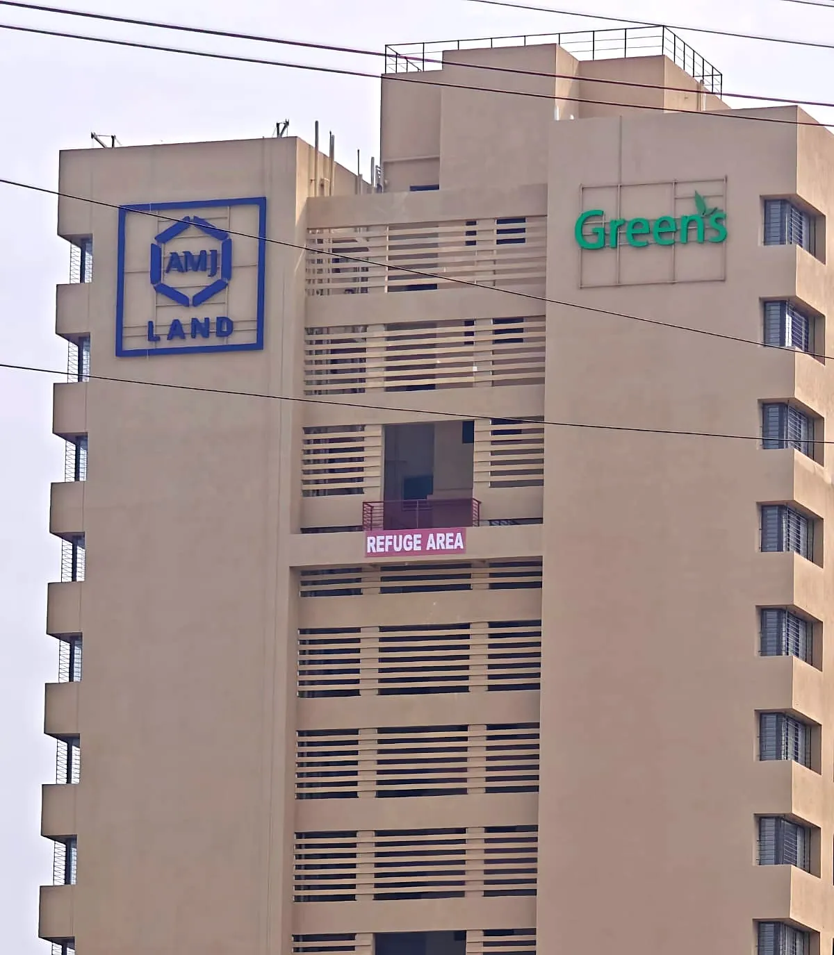 AMJ Land logo and Green’s letters near the top of a residential tower in Pune, by day