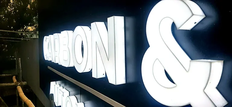 Carbon & Chrome Automotive Studio: white 3D acrylic letters glowing through their faces and sides at night