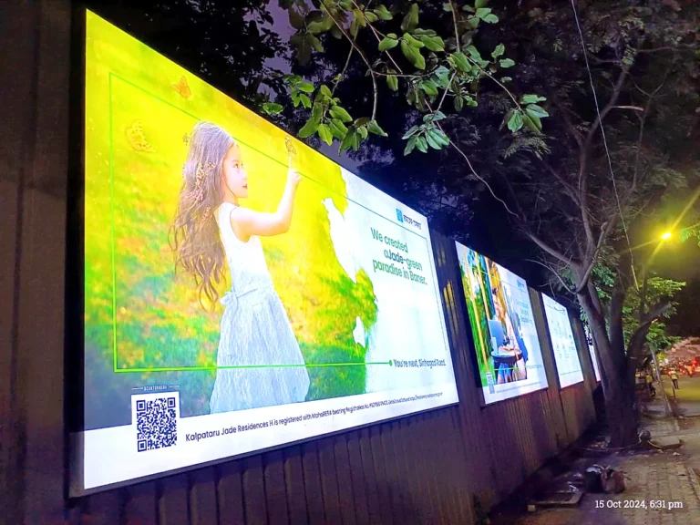 Row of backlit project boards glowing at night on a construction-site fence in Pune