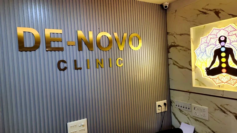 De-Novo Clinic name in gold-finish acrylic letters on a fluted reception wall, with the lit wellness light box
