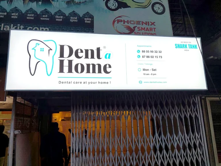 Lit Dent a Home glow sign board above a dental clinic entrance at night