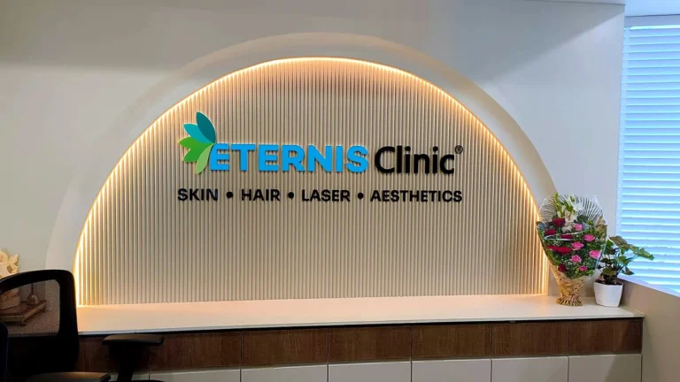 Eternis Clinic reception in Erandwane, Pune: the ETERNIS Clinic logo and SKIN • HAIR • LASER • AESTHETICS in 3D acrylic, fixed straight onto a fluted arched niche lit by an LED strip