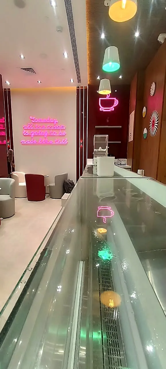 The counter with the pink neon coffee cup on the maroon wall and the neon quote at the far end