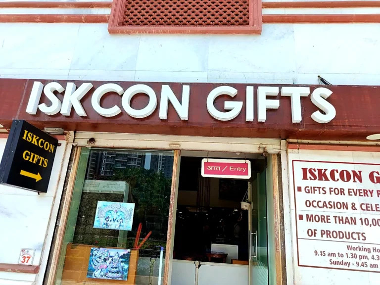 ISKCON GIFTS white acrylic letters by day above the gift shop entrance, with the lit arrow sign pointing to the door