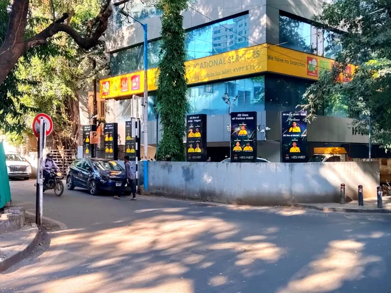 Six backlit boards along the boundary wall of Jha Classes, seen from the road