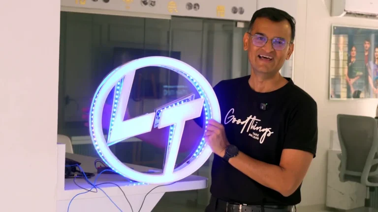 The 2 ft L&T logo sign with its white acrylic face on, lit in colour-changing RGB LEDs, held up in the Orchid Digitals office
