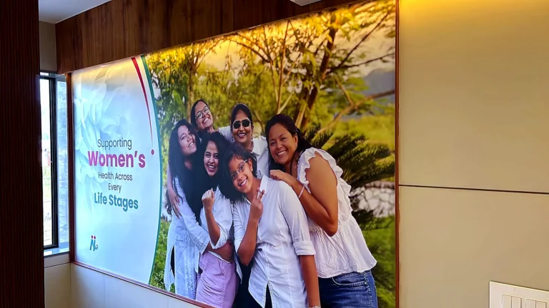 Maternity hospital waiting area in Ahmedabad: wall print of smiling women, Supporting Women’s Health Across Every Life Stage, in a wooden frame