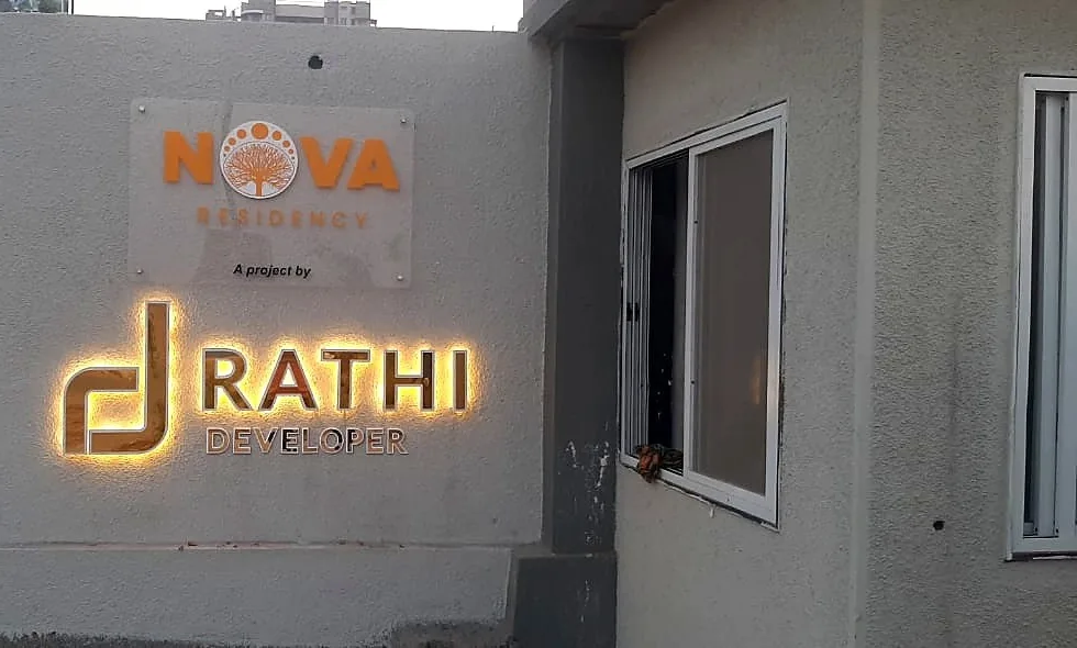 The Nova gate wall at dusk: the clear NOVA plate above and the RATHI DEVELOPER logo glowing warm white from behind