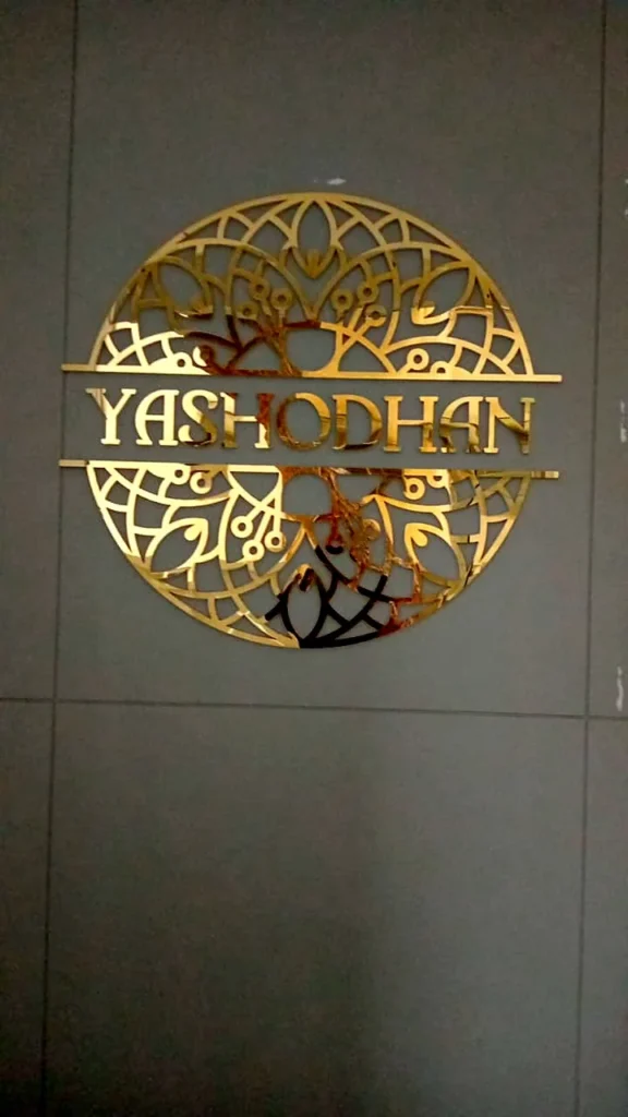 The Yashodhan mandala logo in gold mirror acrylic on the lobby wall, with no base plate