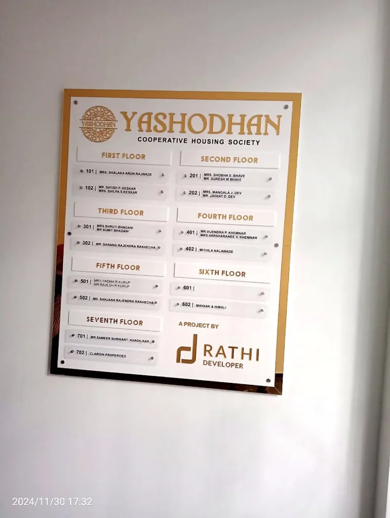 The Yashodhan Co-operative Housing Society name board in the lobby: gold and white acrylic, a name strip for every flat